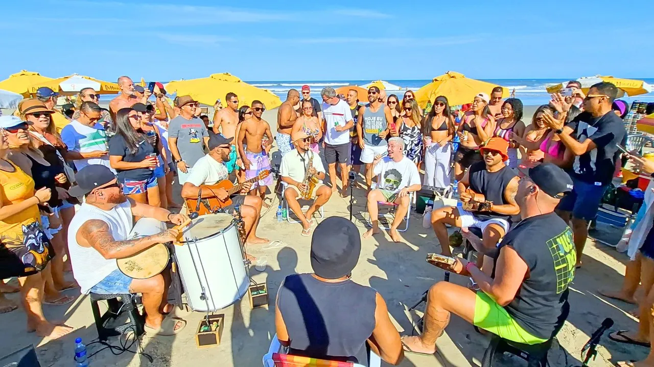 Roda de pagode com vários músicos tocando pandeiro, violão e cavaco na praia
